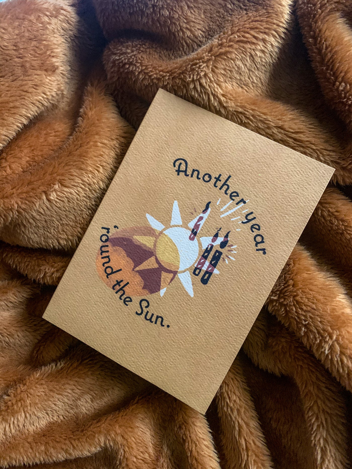 tan colored card that reads "another year around the sun." with sun illustration