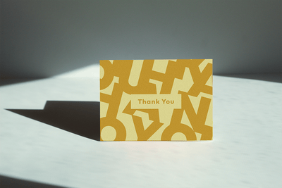 yellow shaded Thank you greeting card thank reads "thank you" and has the letter's of "Thank you" in the background'