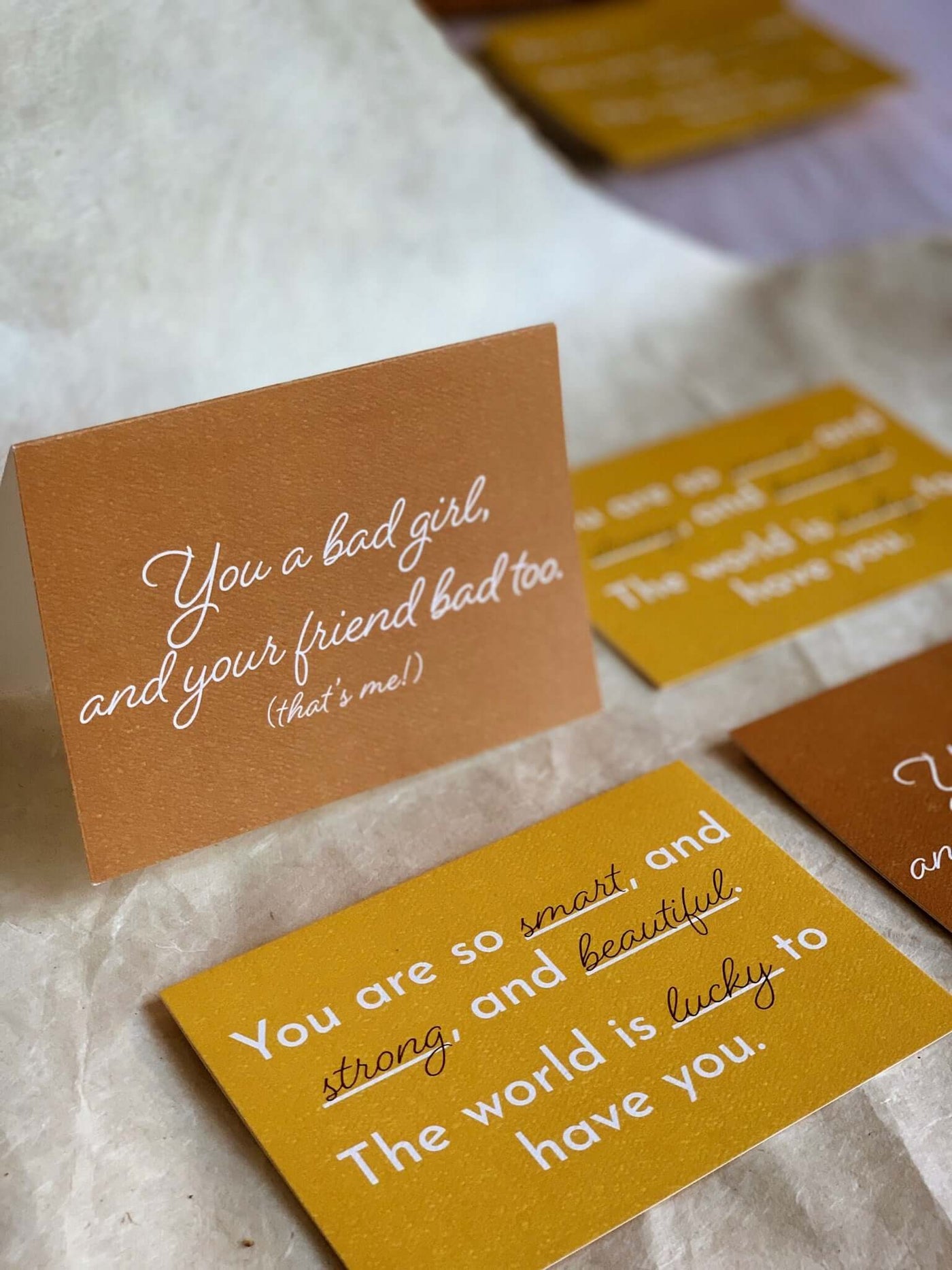 Orange card with a white cursive text that reads 'You a bad girl, and your friend bad too. (that's me!)" and a Yellow card featuring text that says "You are so smart, strong, and beautiful. The world is lucky to have you."
