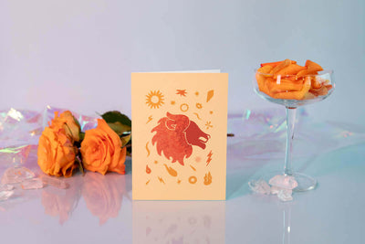 orange flowers behing a yellow leo astrology greeting card with red leo illustration on the cover 
