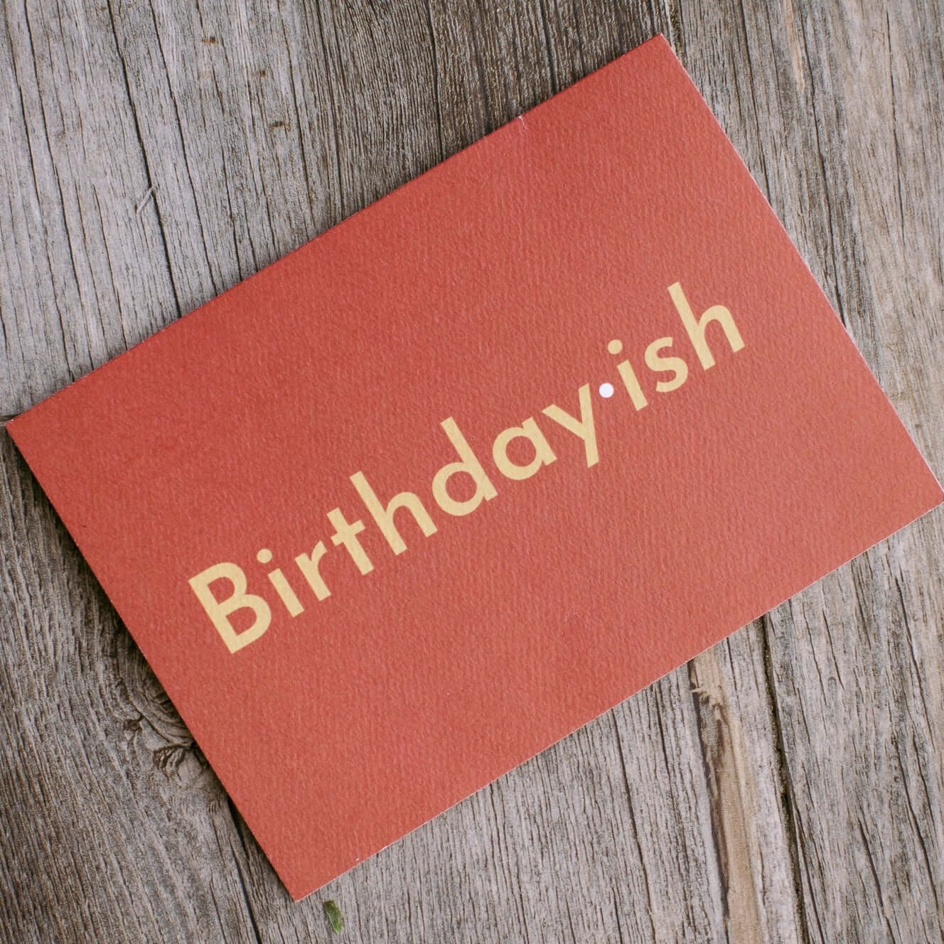 red card that reads "Birthdayish" in tan lettering with a white interpunct between "birthday" and "ish"