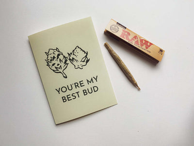 cream colored card that reads "You're my best bud" with marijuana bud illustration as well as Raw rolling papers next to the card.