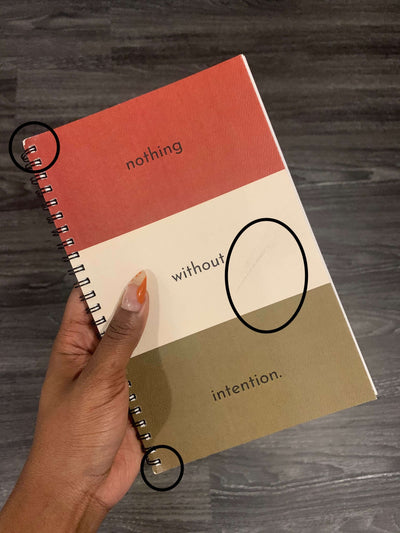 hand holding intention journal that is split into three equal colors of red white and greenish brown that read "nothing", "without", "intention" in each space on the cover