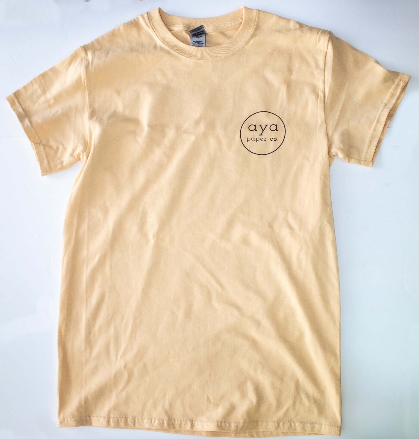 front of the tan colored "Paper Chasers T-Shirt" that has the Aya Paper Co. logo on the chest