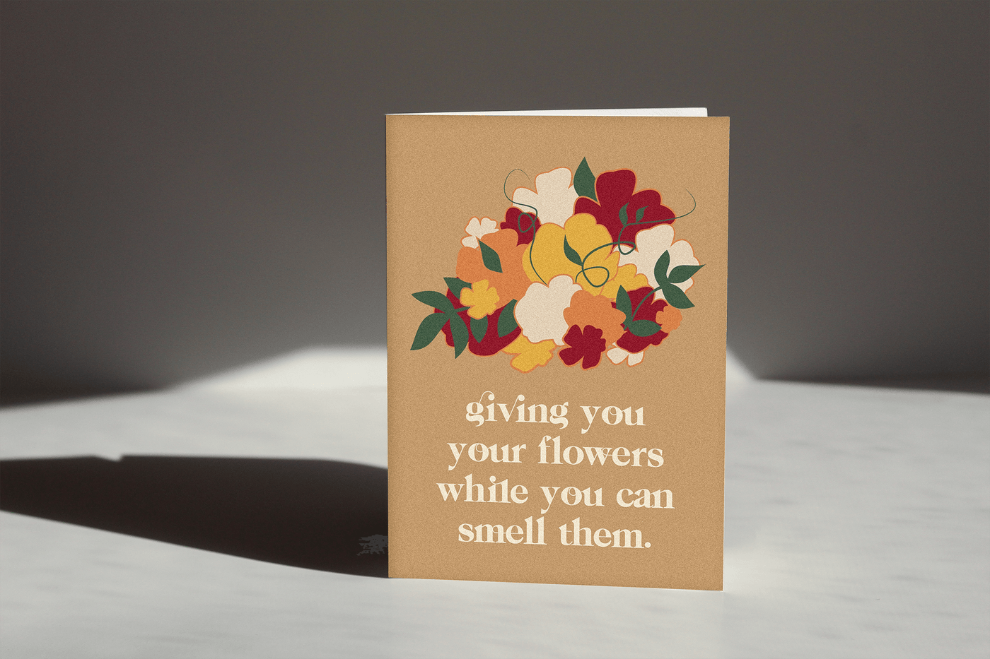 sand colored card that reads "giving you flowers while you can smell them" with an illustration of a flower bouquet