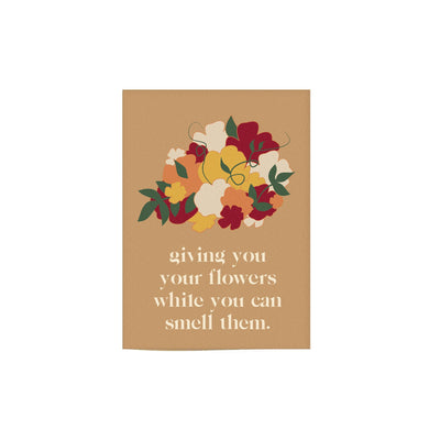 sand colored card that reads "giving you flowers while you can smell them" with an illustration of a flower bouquet,