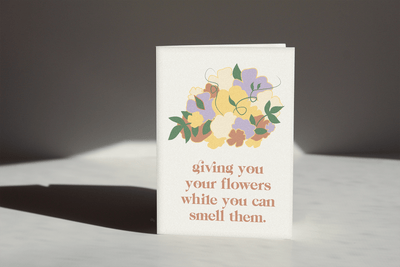cream colored card that reads "giving you flowers while you can smell them" with an illustration of a flower bouquet