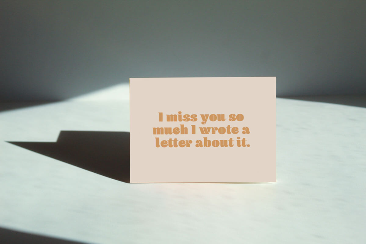 beige horizontal card that reads "I miss you so much I wrote a letter about it". in a yellow brownish text on a counter.